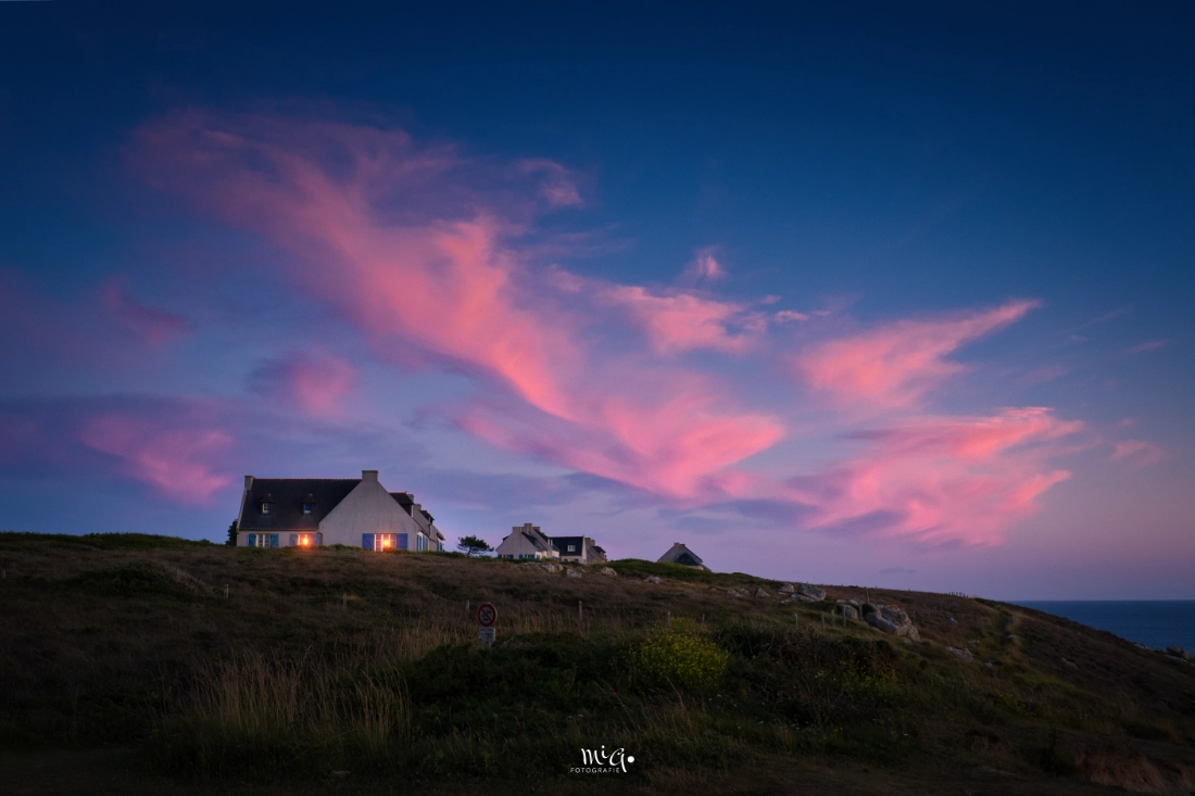 Rosa Flammen ueber der Crozon-Halbinsel Bretonisches Kuestenhaus auf der Presqu'île de Crozon unter einem dramatischen Abendhimmel mit leuchtend rosa Wolken ueber dem Atlantik in der Bretagne