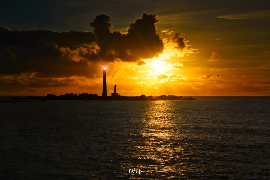 Silhouette des Leuchtturms Île Vierge in der Bretagne vor einem dramatischen Sonnenuntergang mit goldenem Lichtspiel auf dem Atlantik