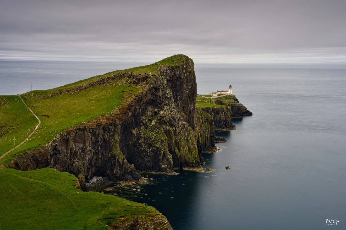 Leuchtturm Neist Point auf einer dramatischen Felsklippe der Isle of Skye in Schottland mit ruhigem grauem Meer und sattem grünen Grasland