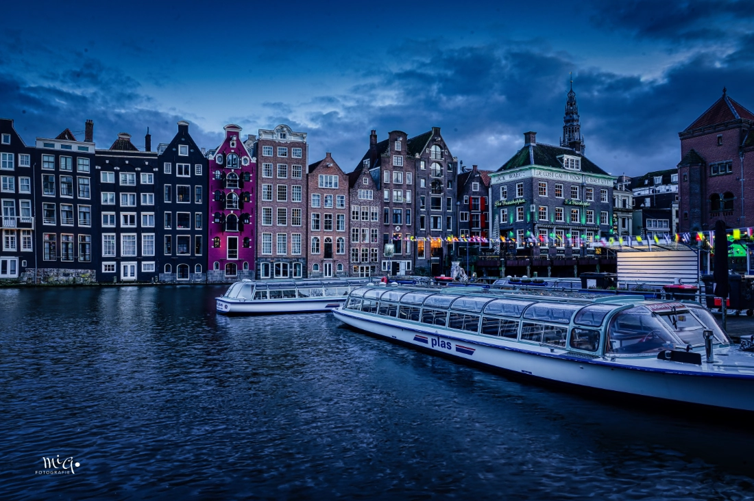 Historische Grachtenhäuser in Amsterdam in der Dämmerung mit Rundfahrtbooten im Vordergrund, aufgenommen als HDR-Stadtfotografie.