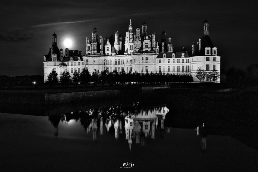 Nächtliche Ansicht von Schloss Chambord in Frankreich mit Mondschein und Spiegelung im Wasser, in einer kontrastreichen Schwarz-Weiß-Fotografie.