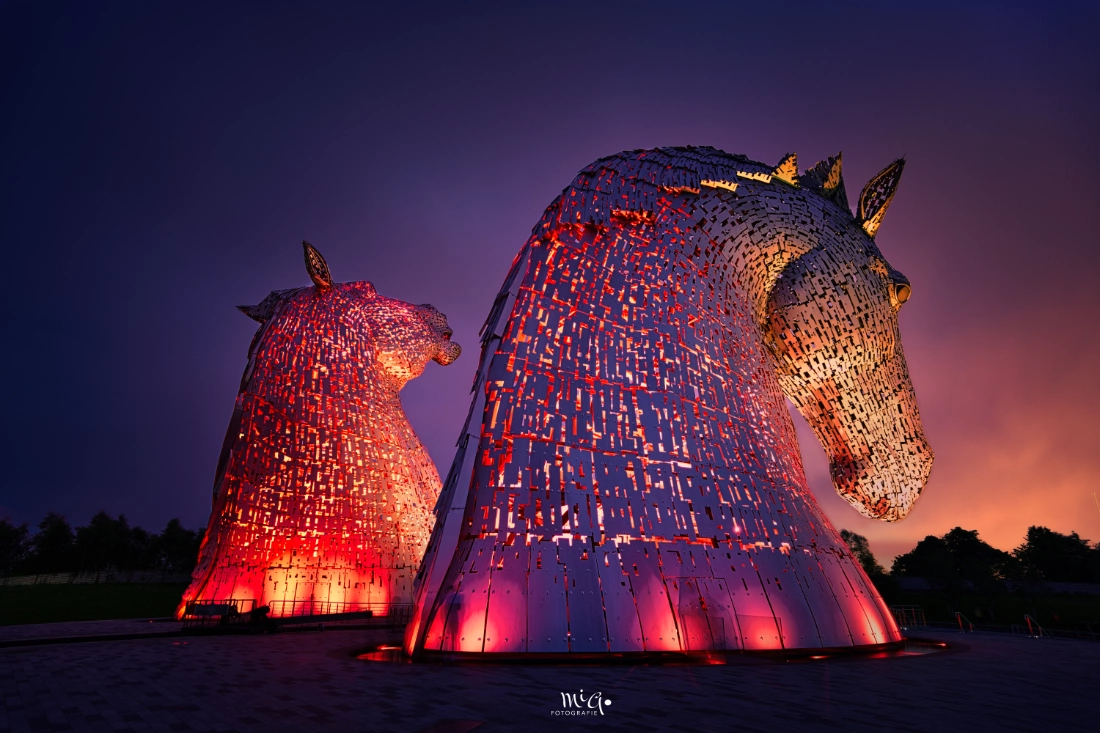 Die monumentalen Kelpies-Stahlskulpturen in Schottland, beleuchtet in intensiven Farben während der Dämmerung, als Architekturfotografie.